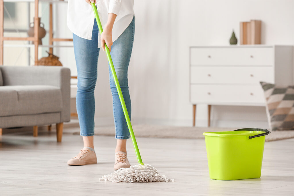 A cleaner mopping the floor of an empty, sunlit room during a move-out cleaning